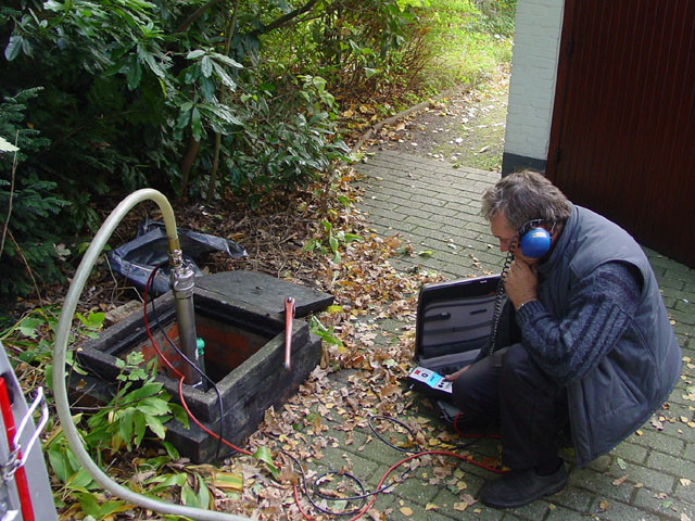 Technieker met gehoorbescherming bij een open inspectieput tijdens de lekdichtheidscontrole